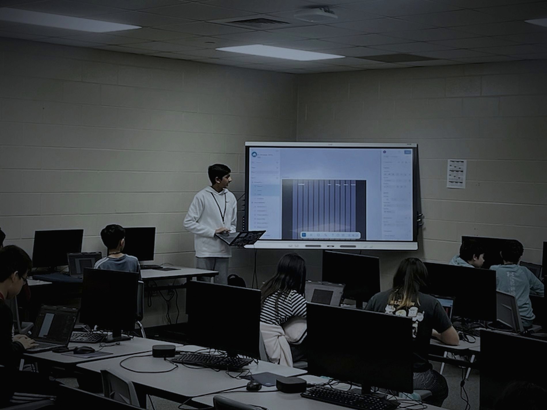 Aariv Patel teaching a design lesson at the front of a computer lab while students work at their screens